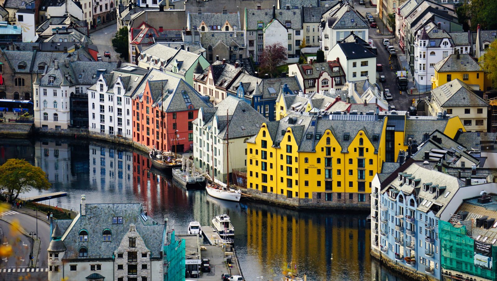 Jugendhusene langs Brosundet i Ålesund sett ovenfra, med seilskuter ved kai og speiling i vannet