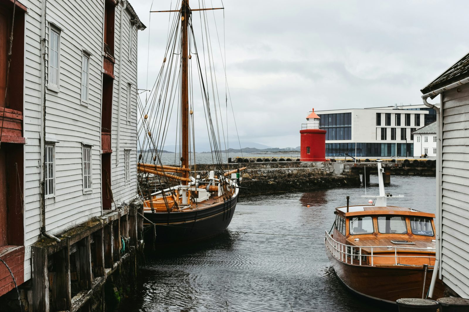 Det lille røde Molja fyr ved moloen i Ålesund, med trebåter og gamle sjøhus i forgrunnen
