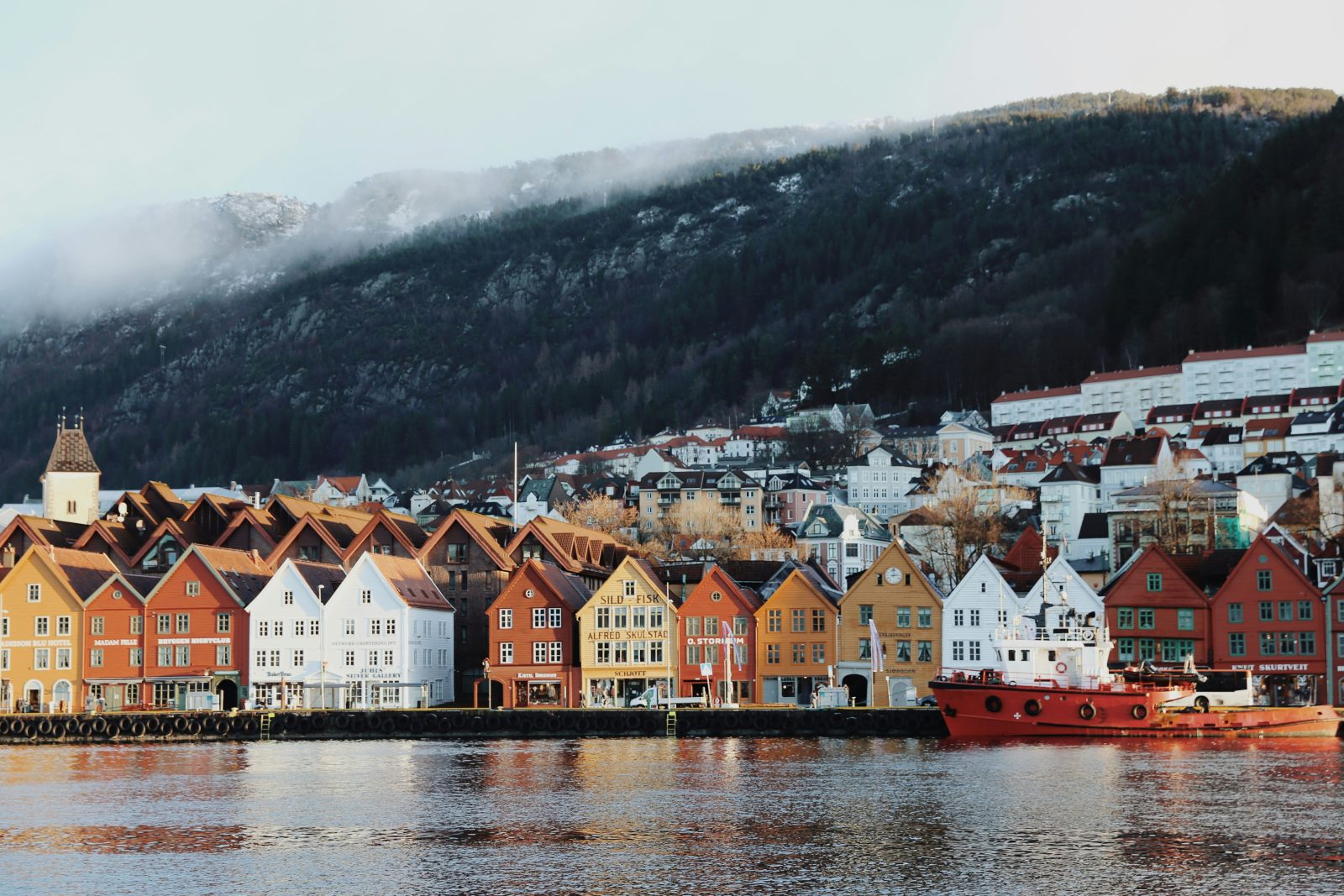 Den fargerike trehusrekken på Bryggen i Bergen sett over Vågen, med tåke over byfjellet bak