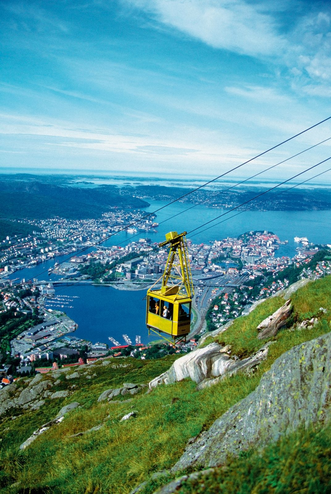 Den gule Ulriksbanen-gondolen på vei opp fjellsiden, med Bergen, Byfjorden og øyene i bakgrunnen