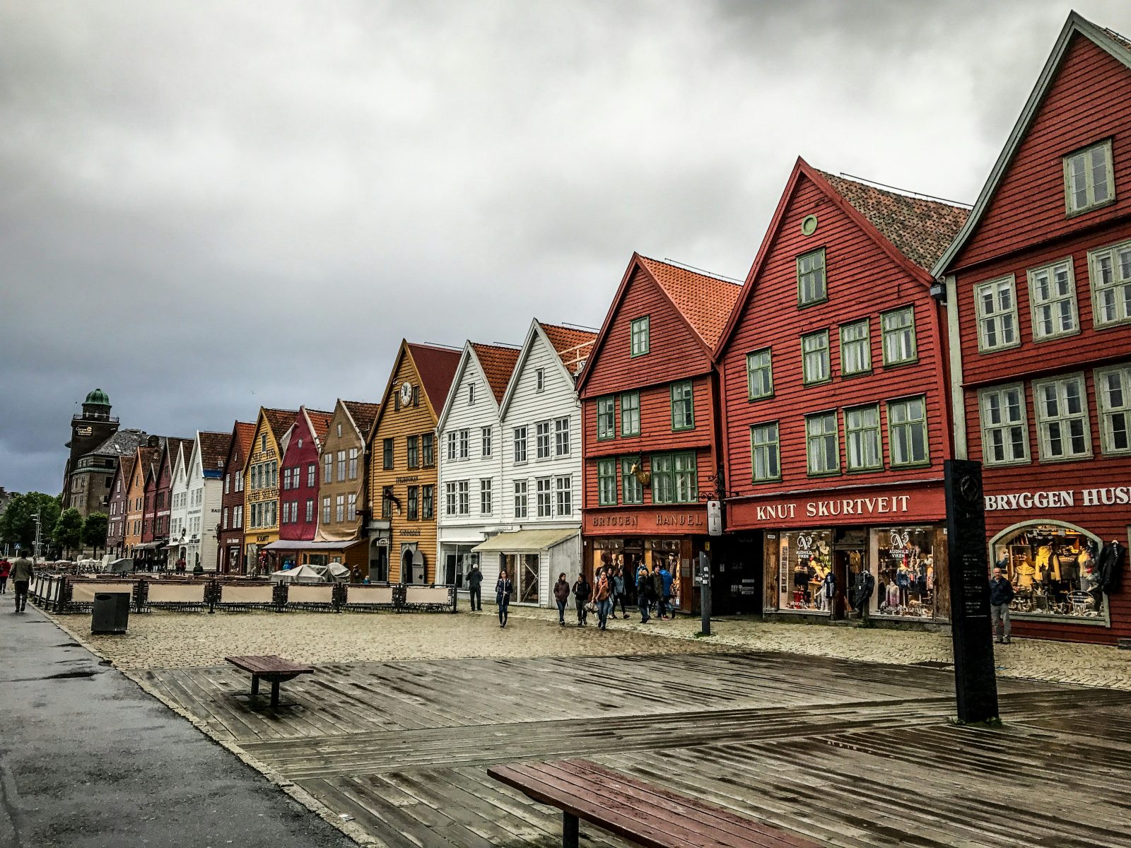 Hele trehusrekka på Bryggen sett fra plassen foran, med butikker i første etasje og regnvått brostein