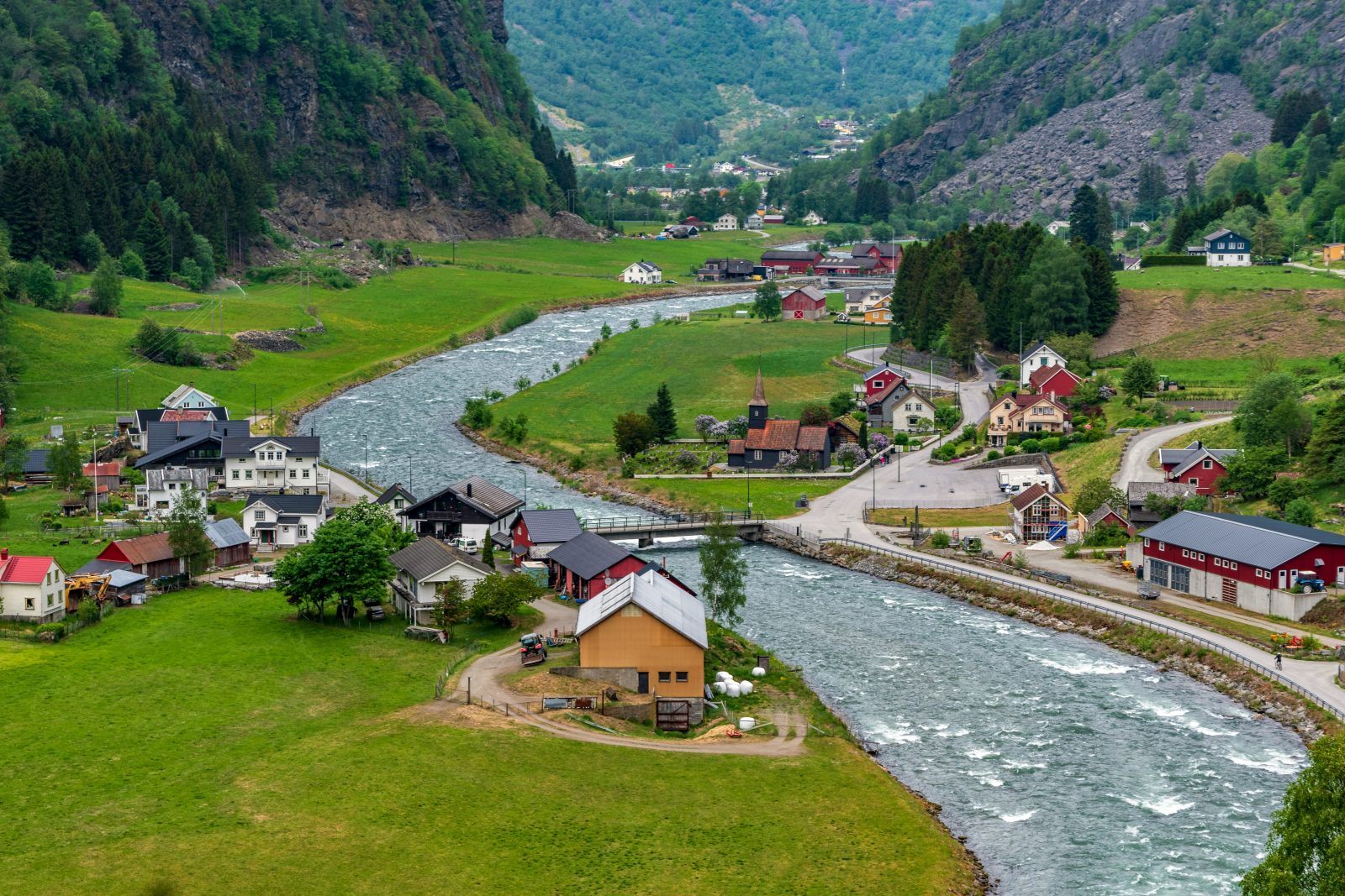 Flåmsdalen med elva som renner gjennom bygda, den mørke trekirka Flåm kyrkje og gårder på grønne jorder