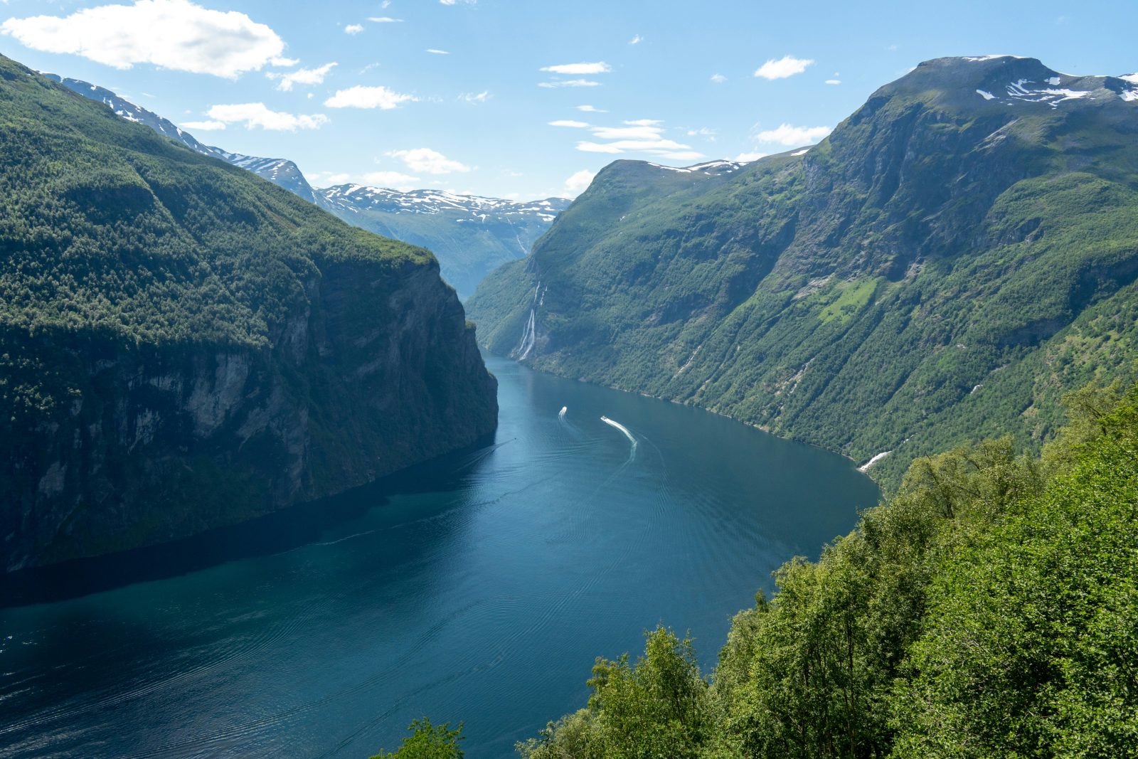 Geirangerfjorden sett fra Ørnesvingen, med båter på det blågrønne vannet mellom bratte, grønne fjellsider