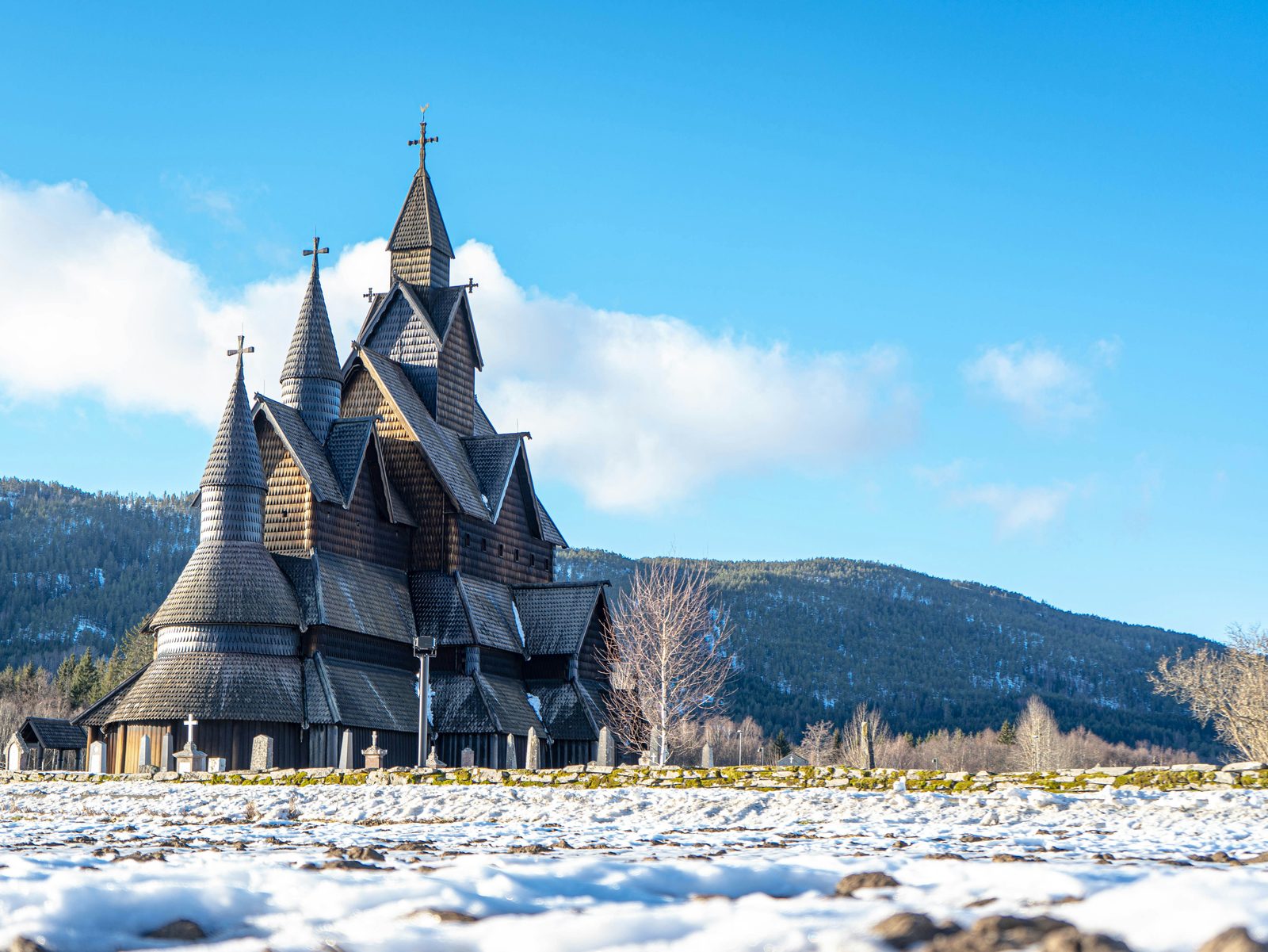 Heddal stavkirke en klar vinterdag med snø på bakken og blå himmel bak de mørke spirene