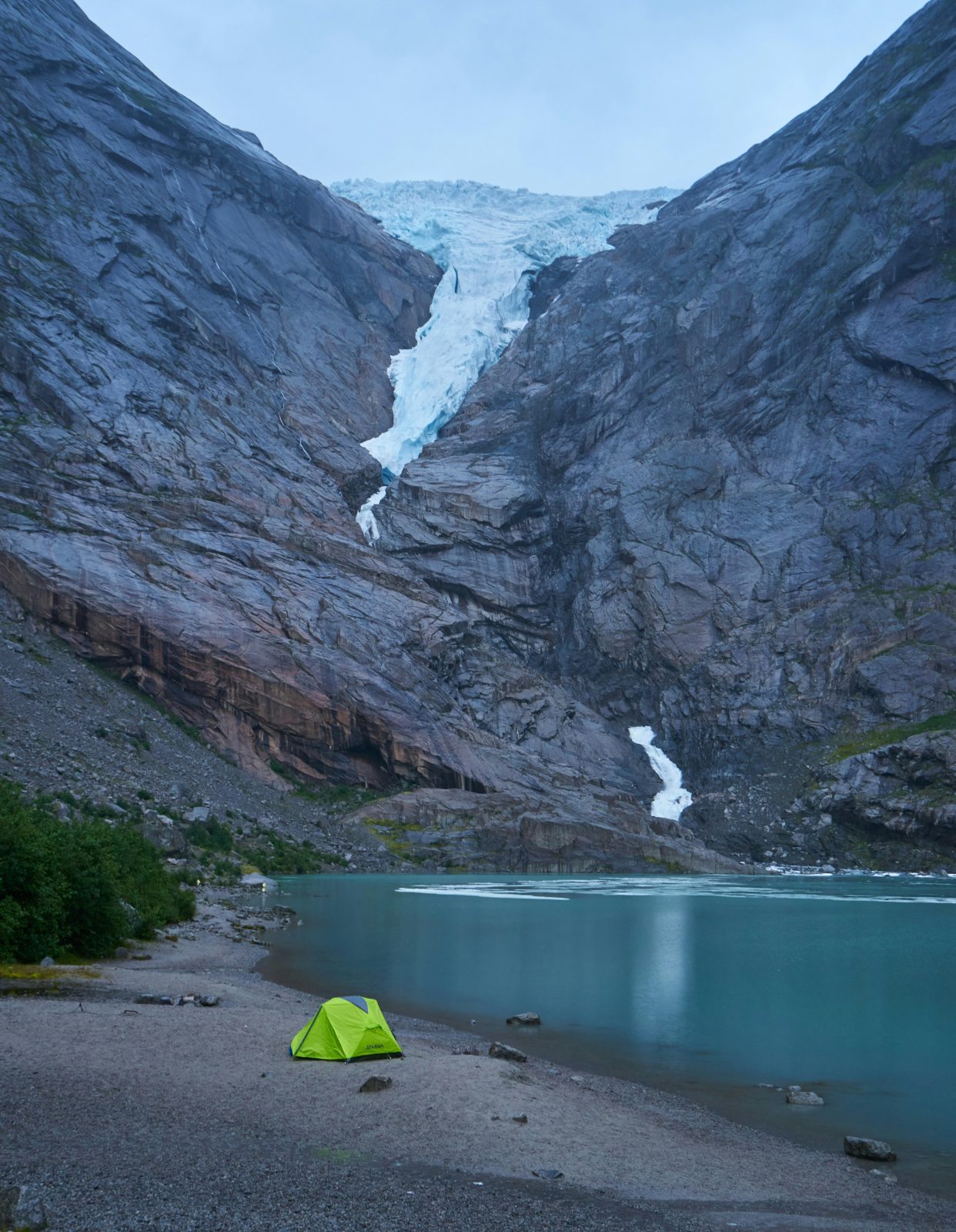 Grønt telt ved bredden av det turkise brevannet under Briksdalsbreen i kveldslys