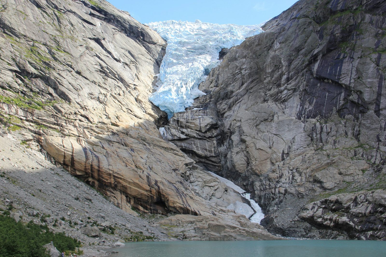 Briksdalsbreen henger blåhvit i fjellskaret over den grønne bresjøen en klarværsdag