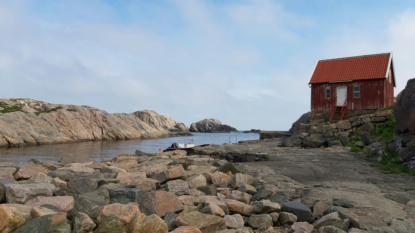 Rød sjøbu på svaberg ved en stille vik i skjærgården ved Lindesnes
