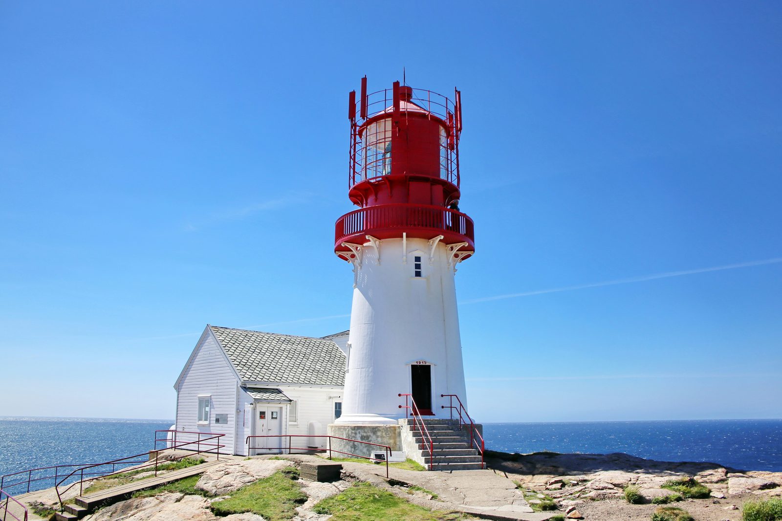 Lindesnes fyr i solskinn – det rød-hvite støpejernstårnet fra 1915 med fyrvokterboligene rundt