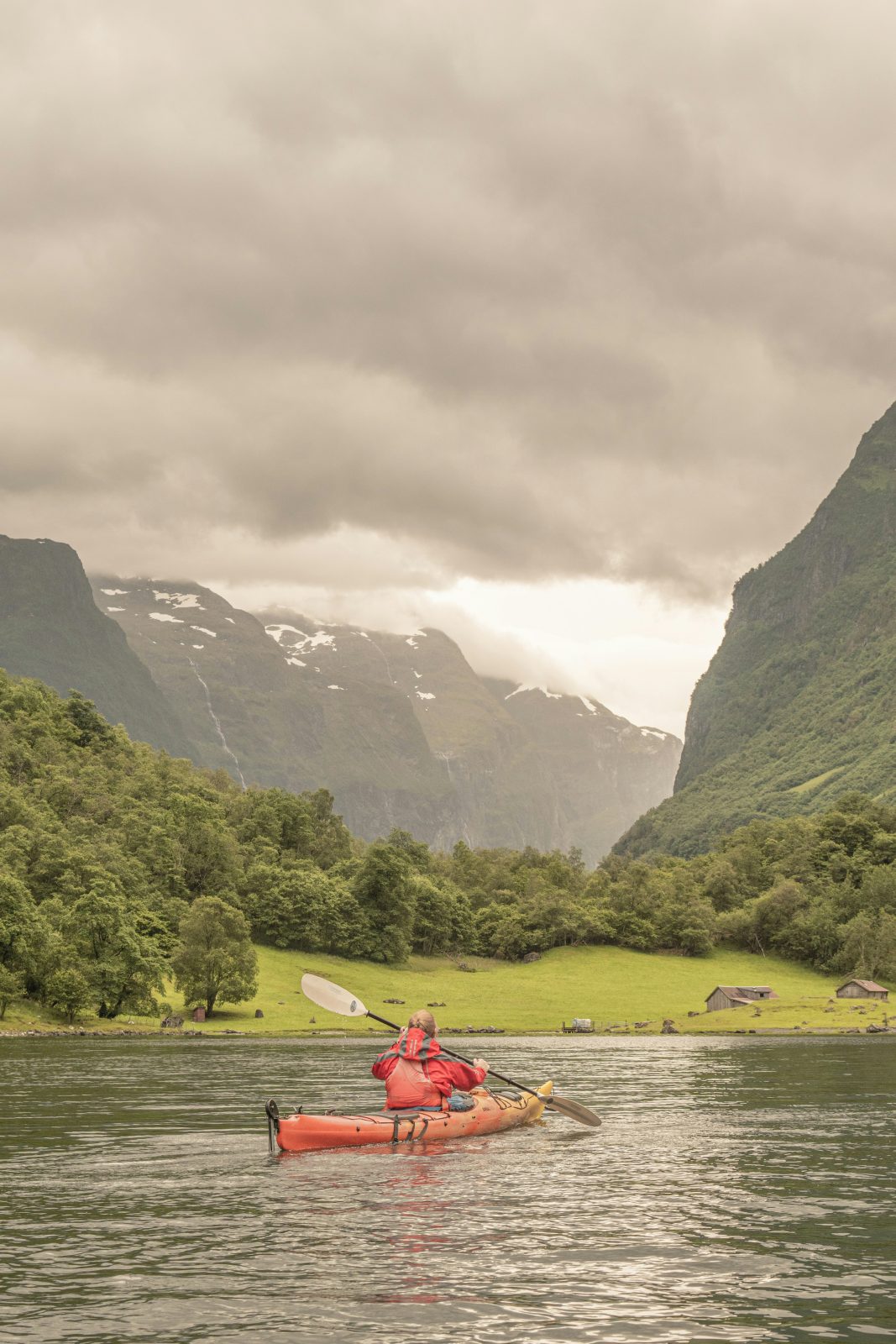Padler i rød kajakk på Nærøyfjorden ved Gudvangen, med fossefall og bratte fjellsider foran