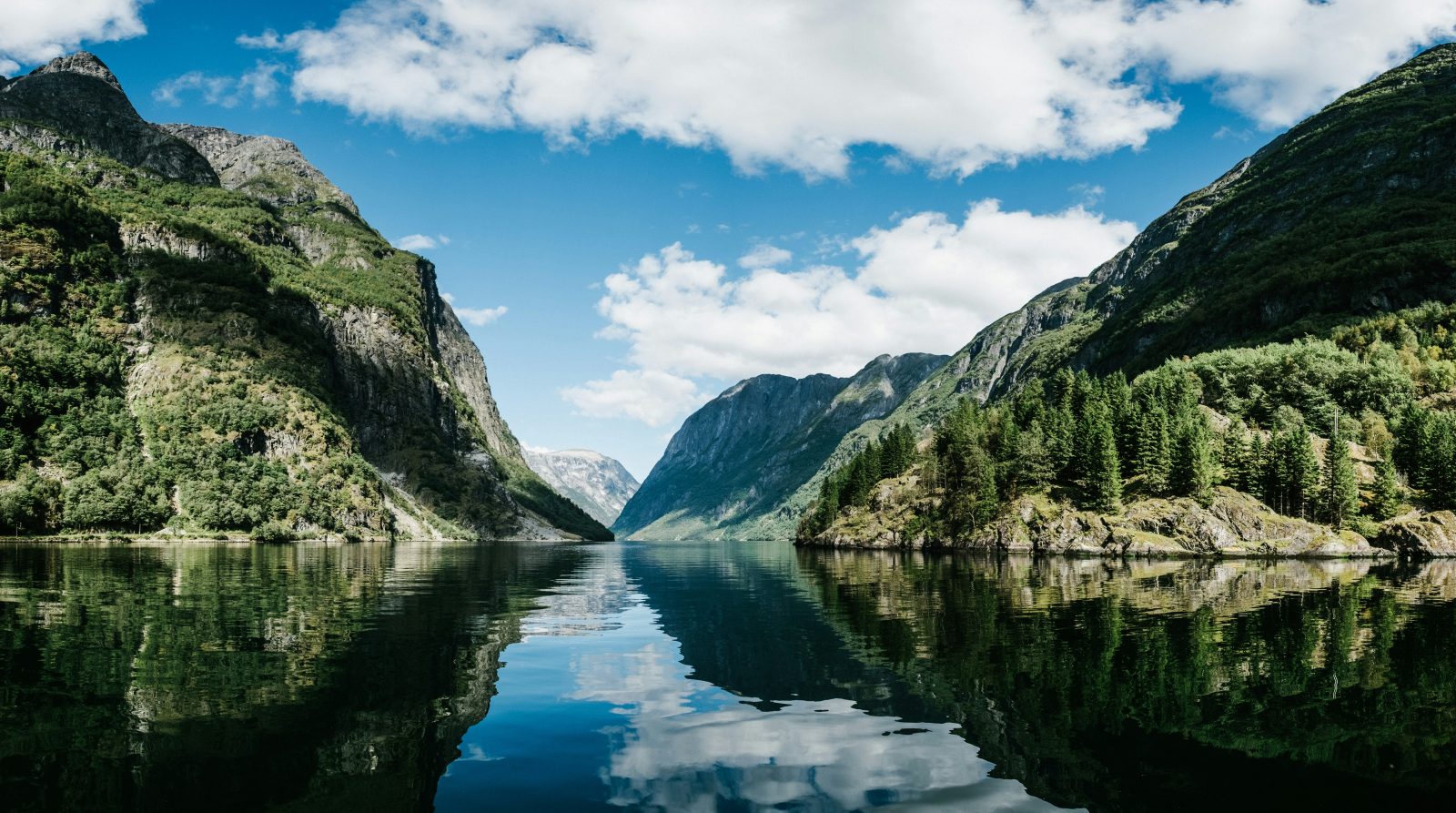Nærøyfjorden ved Gudvangen med fjellsidene speilet i blikkstille vann under blå himmel