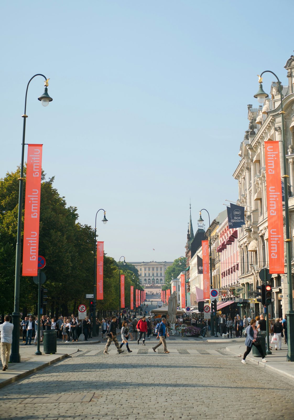 Karl Johans gate med røde bannere og folkeliv, med Slottet i enden av gata