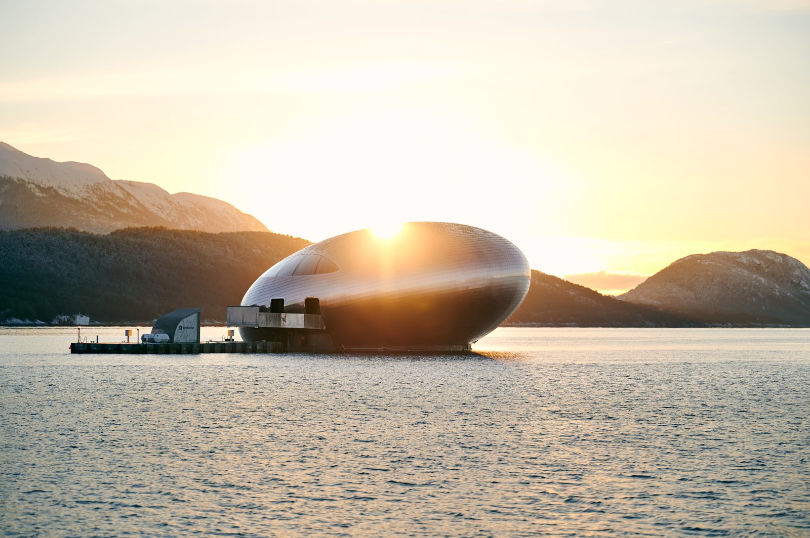 Salmon Eye i solnedgang med kaianlegget ved siden av, sola bak lakseøyets silhuett