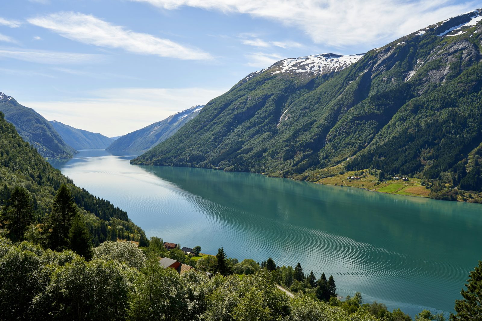 Den grønnturkise fjorden ved Fjærland, med skogkledde fjellsider, snøflekker på toppene og små gårder ved vannet