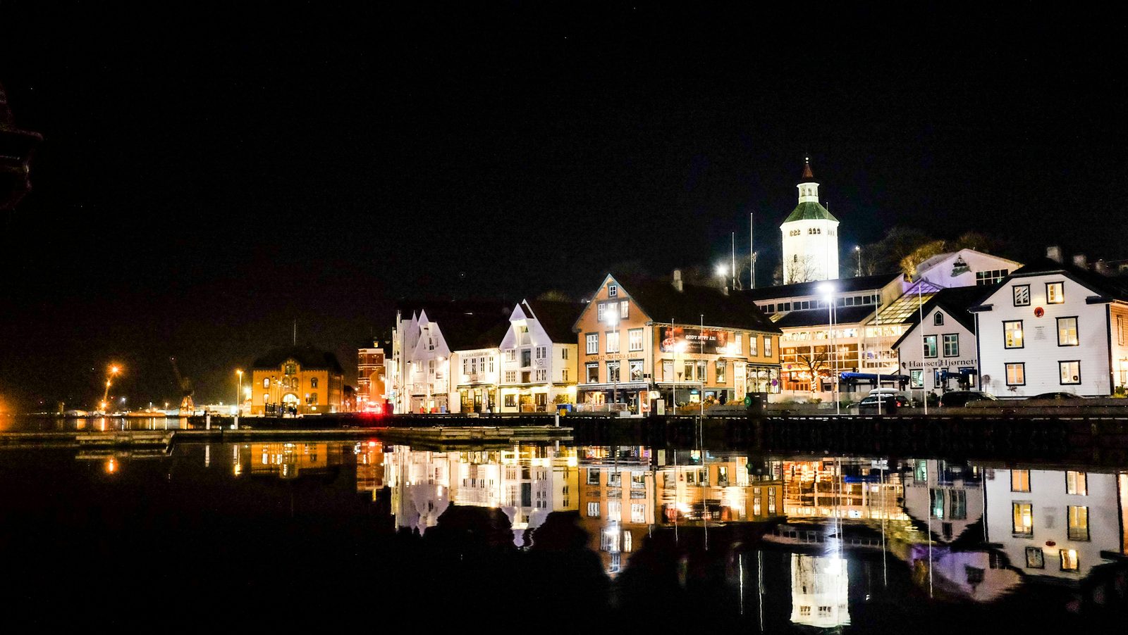 Trehusrekka langs Vågen i Stavanger i kveldslys, med husene speilet i det stille havnebassenget