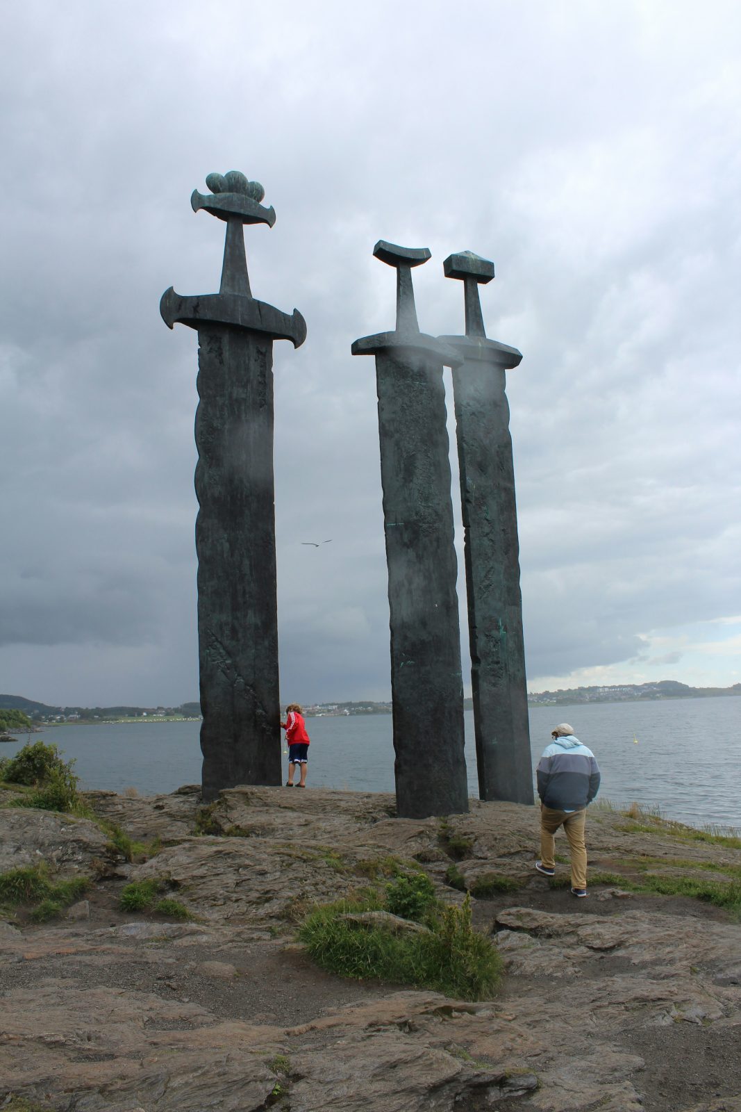 Besøkende ved foten av de tre bronsesverdene i Sverd i fjell, som rager høyt over dem mot grå himmel