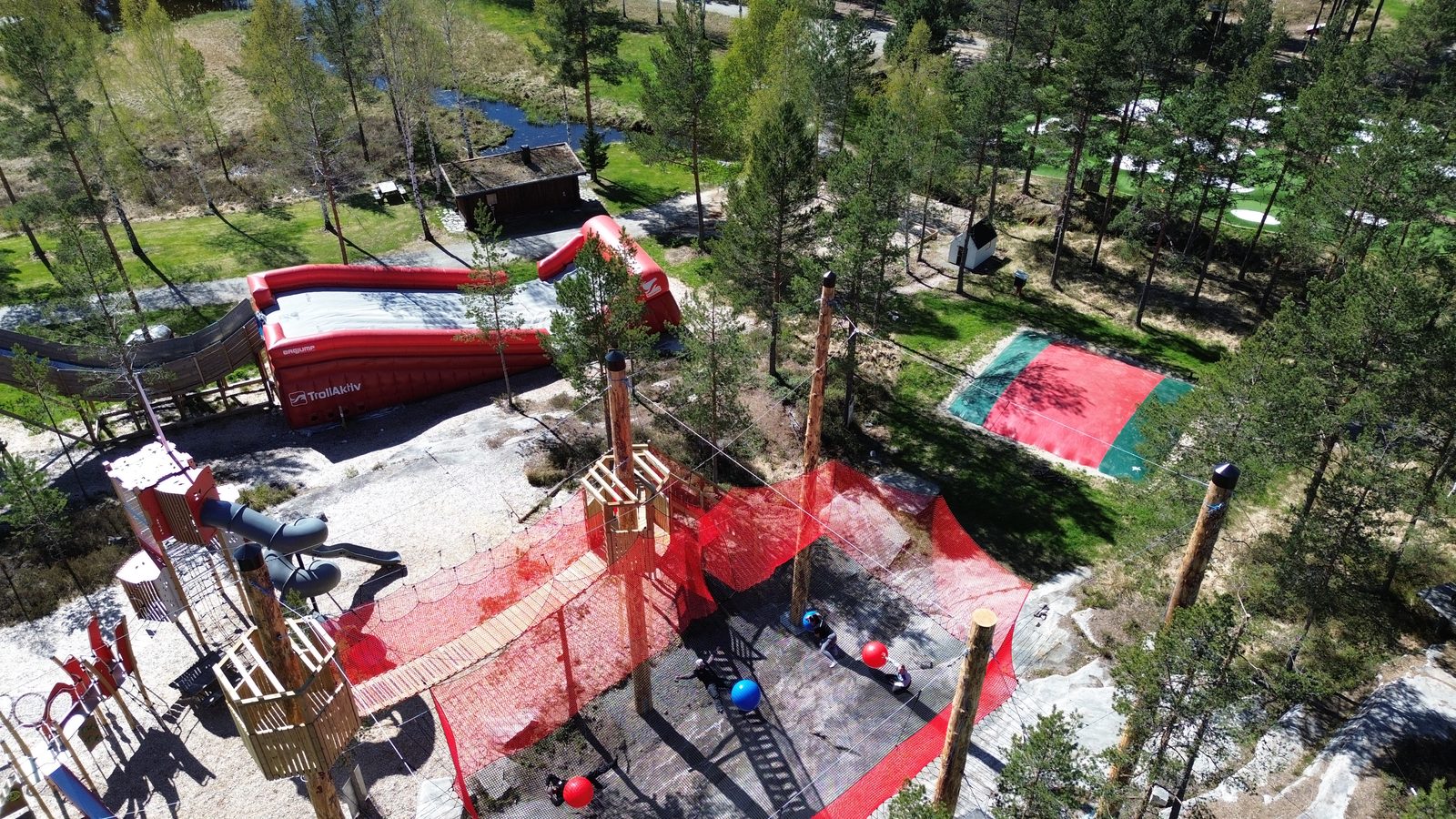 Dronefoto av TrollAktivs aktivitetsområde i furuskogen ved Otra, med sklie, trampoliner og klatreinstallasjoner