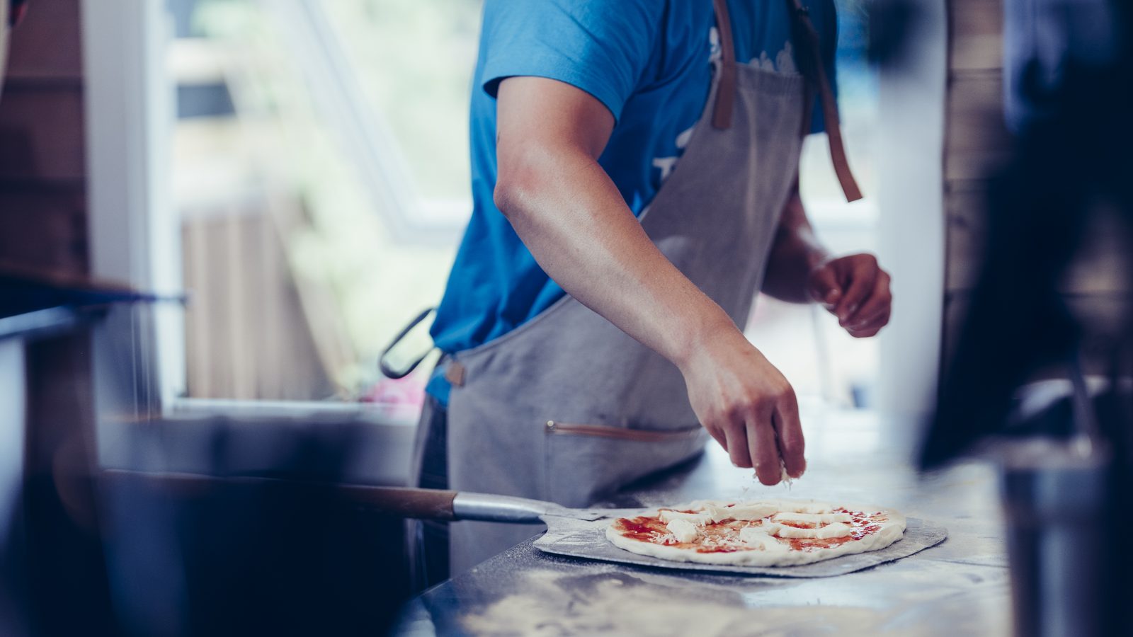 Kokk med forkle legger en hjemmelaget pizza på pizzaspaden i restauranten