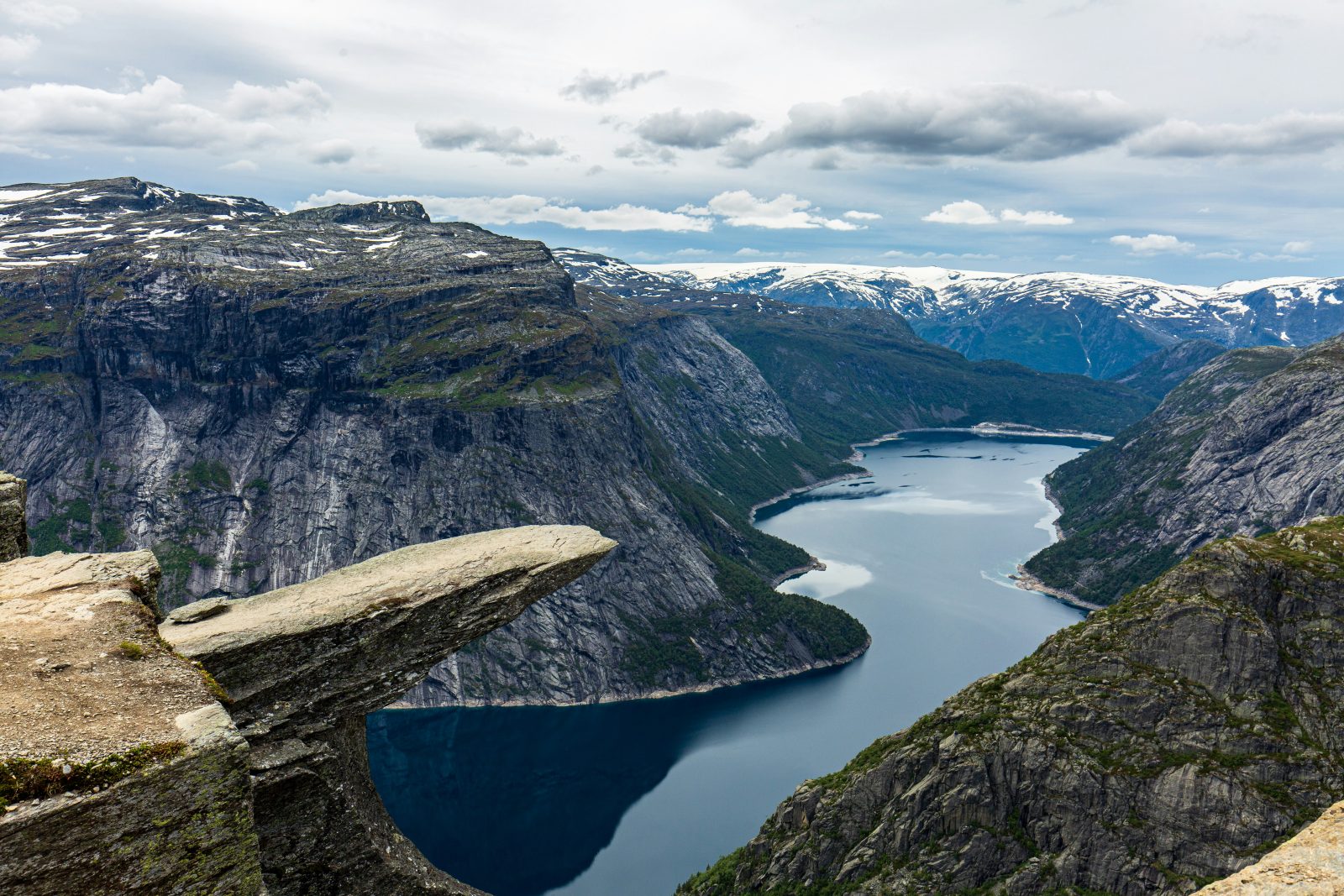 Trolltunga med snødekte fjell og Folgefonna i horisonten, over det mørke Ringedalsvatnet
