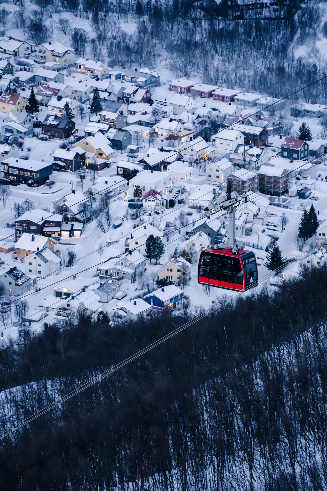 Fjellheisens røde gondol på vei opp over snødekte hustak i Tromsdalen