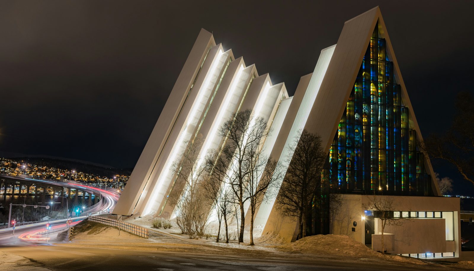 Ishavskatedralen opplyst om kvelden, med den karakteristiske trekantede silhuetten og glassmosaikken