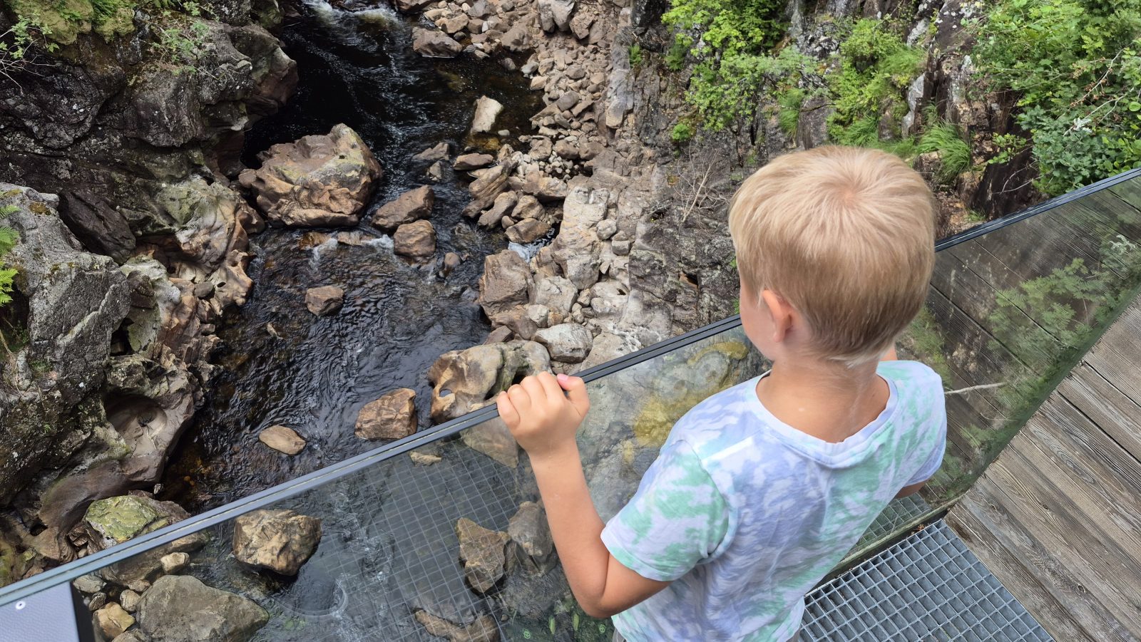 Barn ved glassrekkverket på Planken, med elva og juvet under Kvåsfossen rett nedenfor